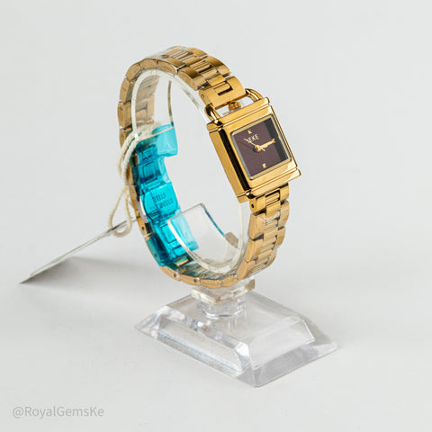 A gold-tone rectangular watch with a dark brown dial and gold hands, displayed on a clear acrylic stand. The watch is wrapped in a blue protective plastic sleeve, and a small tag is attached.
