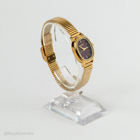A vintage gold-tone watch with a dark brown dial and gold mesh bracelet, displayed on a clear acrylic stand against a white background.