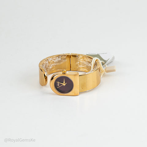 Gold-plated metal cuff bracelet watch with a dark brown dial and gold hands, shown with its retail tags on a white background.