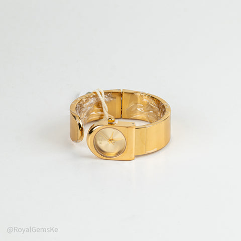 A gold-plated cuff bracelet watch with a square bezel and open dial, shown on a clean white background with a protective plastic wrapper still partially visible inside.