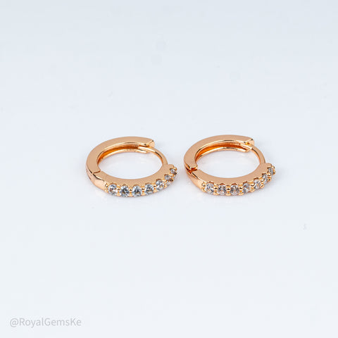 A pair of rose gold huggie hoop earrings with a row of small clear gemstones along the front, displayed on a clean white background.