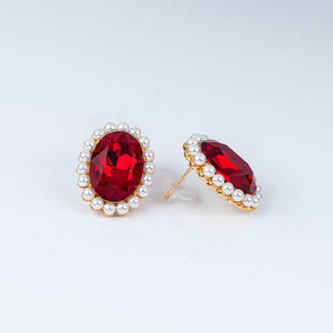 Pair of earrings with red gemstones and pearl-like accents on a light gray background