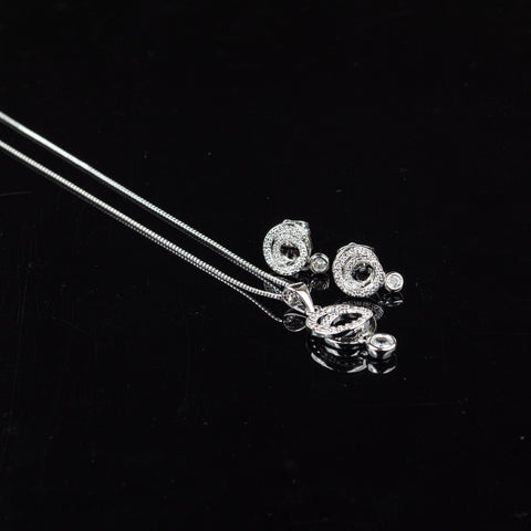 Silver jewelry set including a delicate chain necklace, a circular pendant, and matching stud earrings, displayed on a reflective black surface.