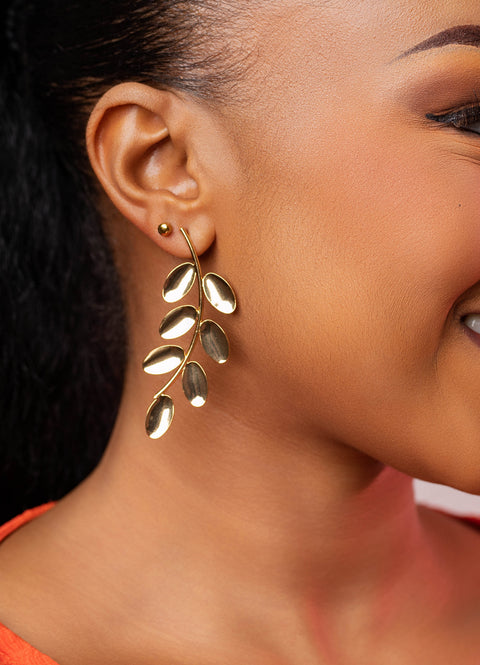 Close-up of a person wearing a gold leaf-shaped earring.