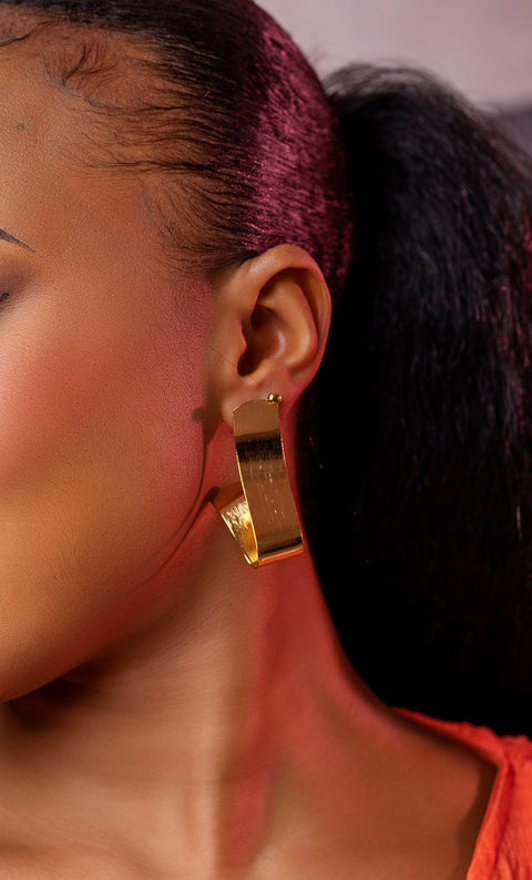 Close-up of a person wearing a gold hoop earring with a blurred background