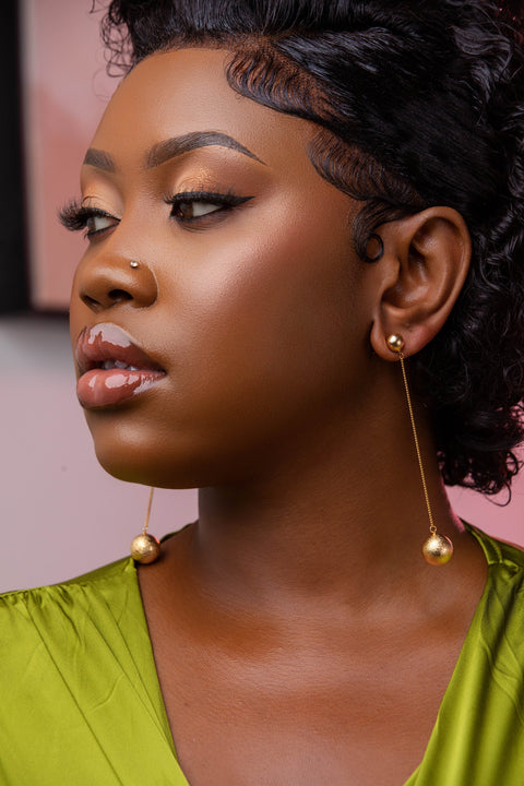 Woman wearing gold earrings with a pink background