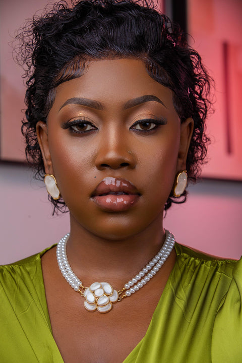Woman wearing a green top and pearl necklace with a blurred background
