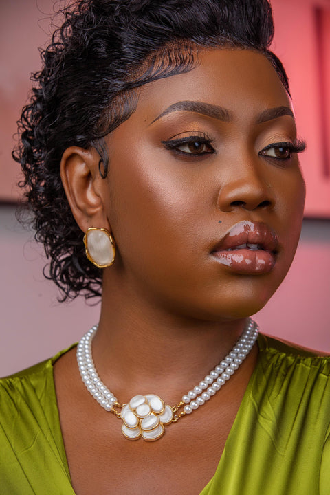 Woman wearing a green top and pearl necklace with a blurred background