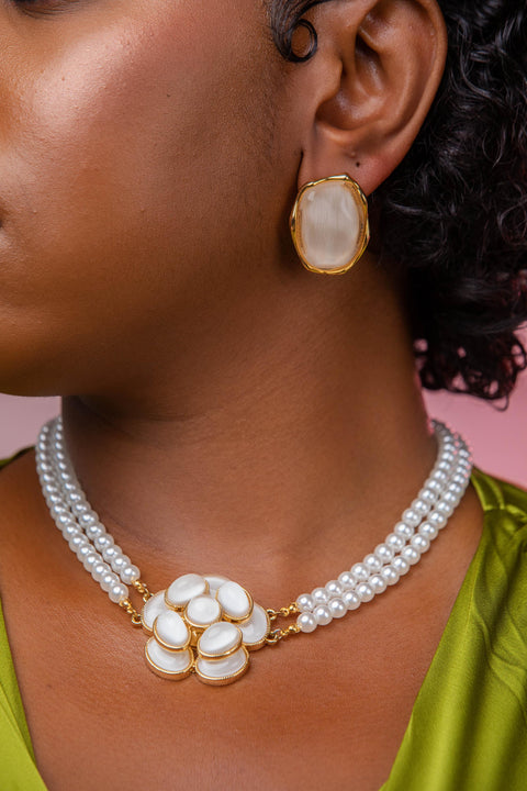 Close-up of a person wearing a pearl necklace and gold earrings against a pink background
