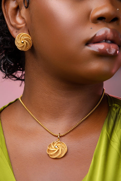 Close-up of a person wearing gold earrings and necklace against a pink background