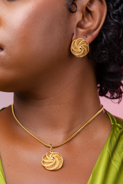 Close-up of a person wearing gold earrings and necklace against a pink background