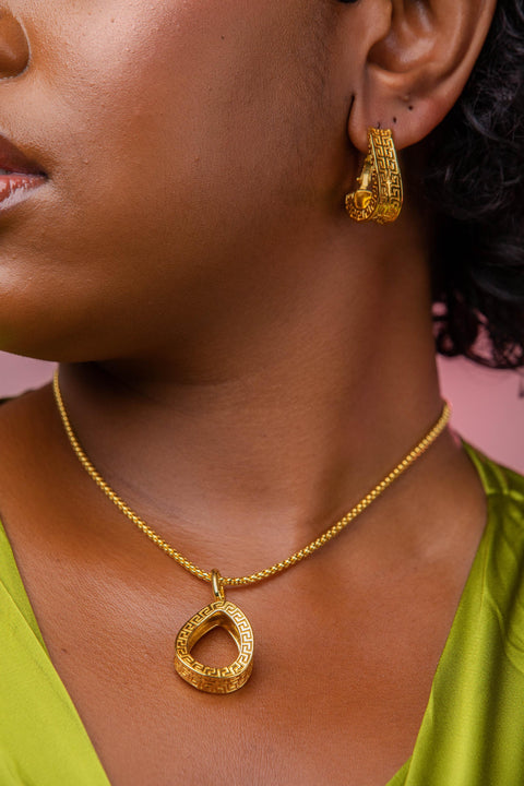 Close-up of a person wearing gold earrings and necklace against a pink background