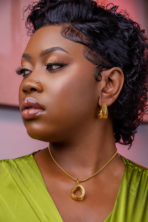 Woman with styled hair wearing a gold necklace and earrings against a pink background