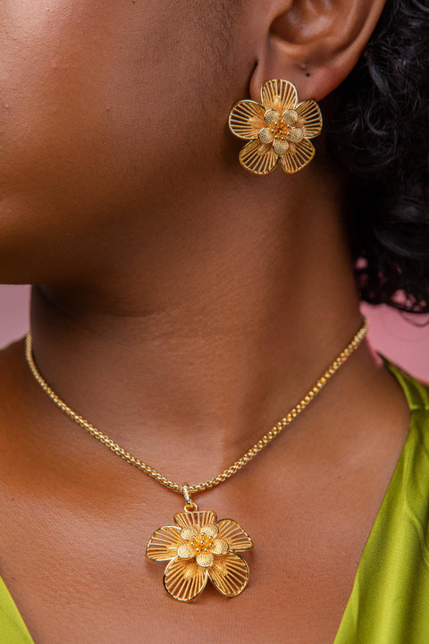 Close-up of a person wearing gold flower earrings and necklace against a pink background