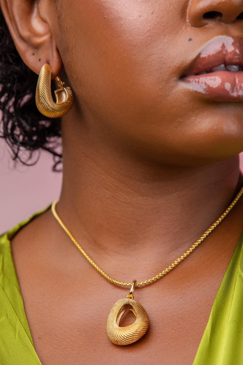 Close-up of a person wearing gold hoop earrings and a gold necklace with a pendant.