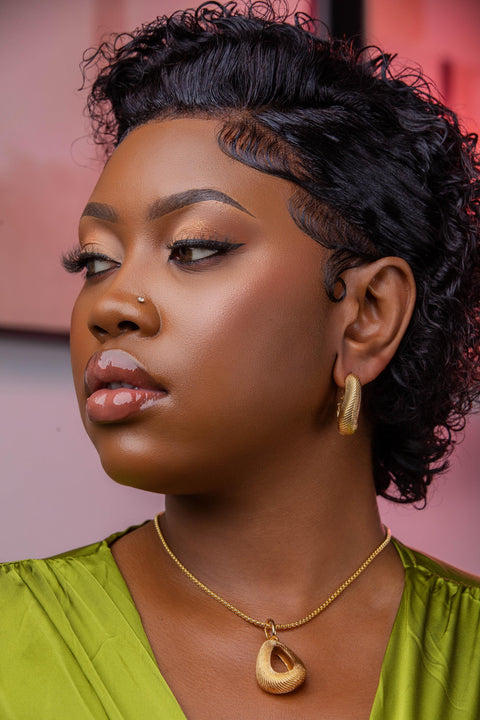 Woman with styled hair wearing a green top and gold necklace against a pink background