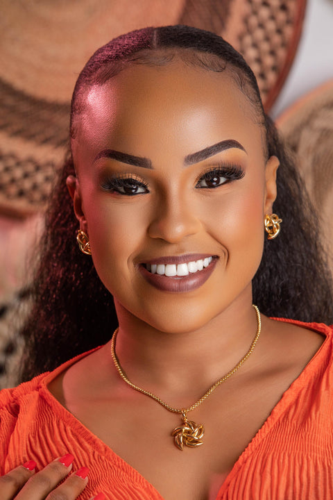 Woman wearing an orange top with gold jewelry against a blurred background