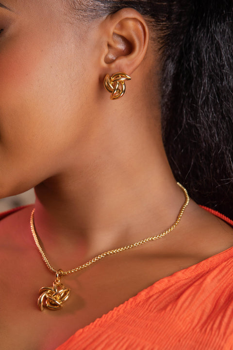 Close-up of a person wearing gold earrings and necklace with an orange top.