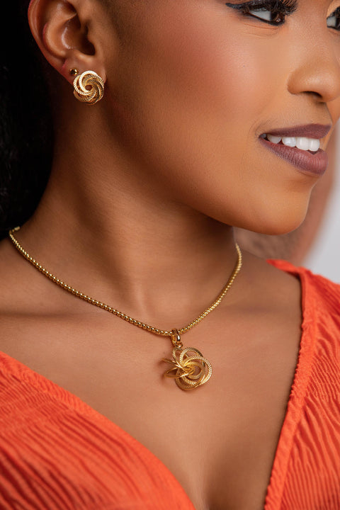 Woman wearing a gold necklace and earrings with an orange top.