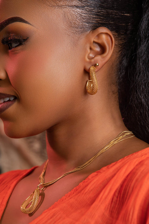 Close-up of a woman wearing gold earrings and necklace with an orange top.
