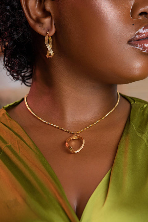 Close-up of a person wearing a gold necklace and earrings with a green top.