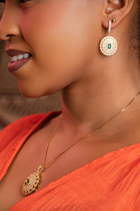 Close-up of a woman wearing gold earrings and necklace with green gemstones.