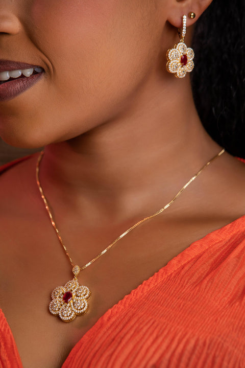 Close-up of a woman wearing gold floral earrings and necklace with red gemstones.