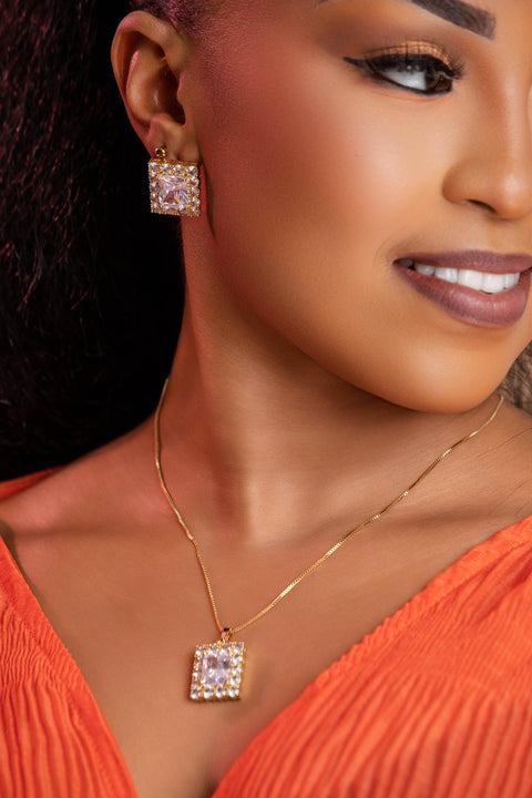 Close-up of a woman wearing diamond earrings and a necklace with a square pendant.