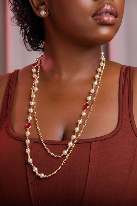 Woman wearing a pearl and red bead necklace with a blurred background