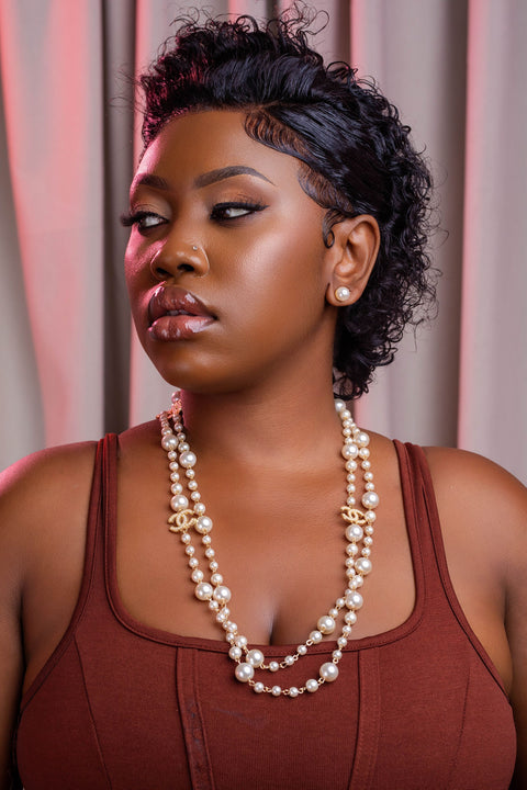 Woman wearing a pearl necklace and a brown top against a neutral background