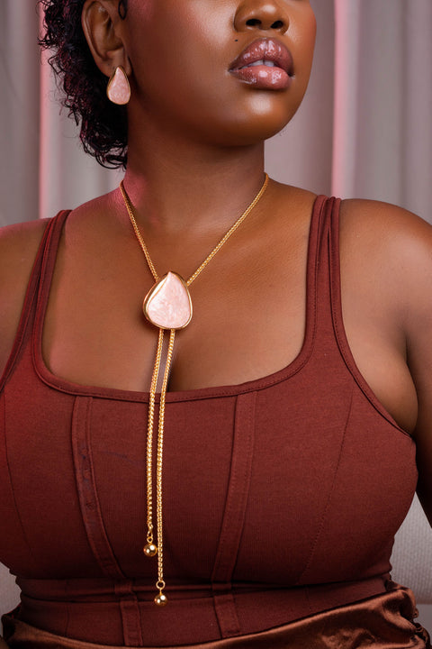 Woman wearing a gold necklace with a heart-shaped pendant against a neutral background