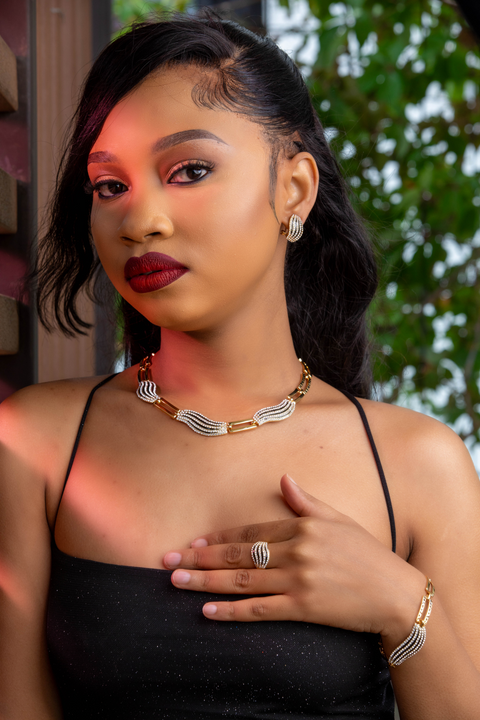 Woman wearing a black top and gold jewelry with a blurred outdoor background