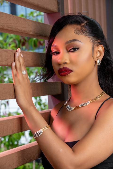 Woman with makeup and jewelry leaning against a wooden railing outdoors