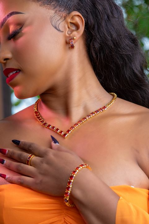 Woman wearing a gold necklace, bracelet, and ring with a blurred outdoor background