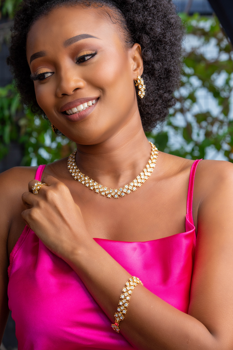 Woman wearing gold jewelry with a pink top against a blurred natural background