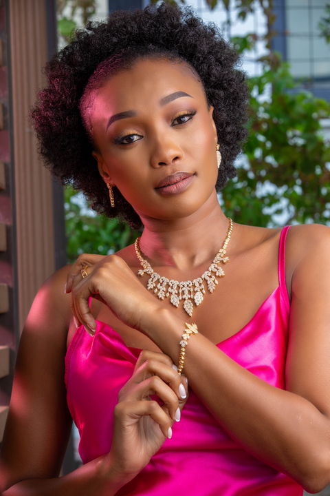 Woman in a pink dress with jewelry, sitting outdoors.