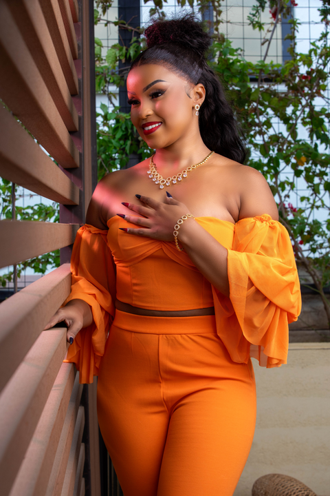 Woman in an orange outfit standing outdoors with greenery in the background