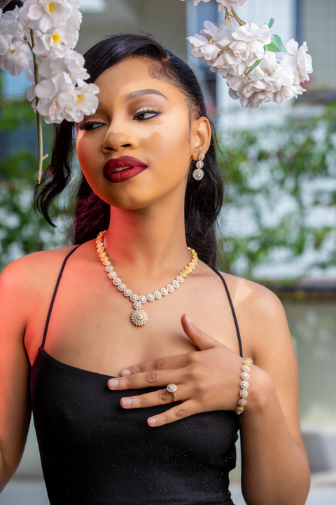 Woman wearing a black dress with jewelry, surrounded by flowers.