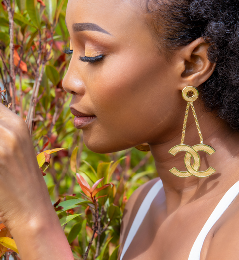 Woman wearing gold earrings and bracelet with a blurred natural background