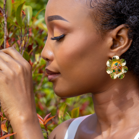 Woman wearing gold jewelry with a floral earring against a natural background