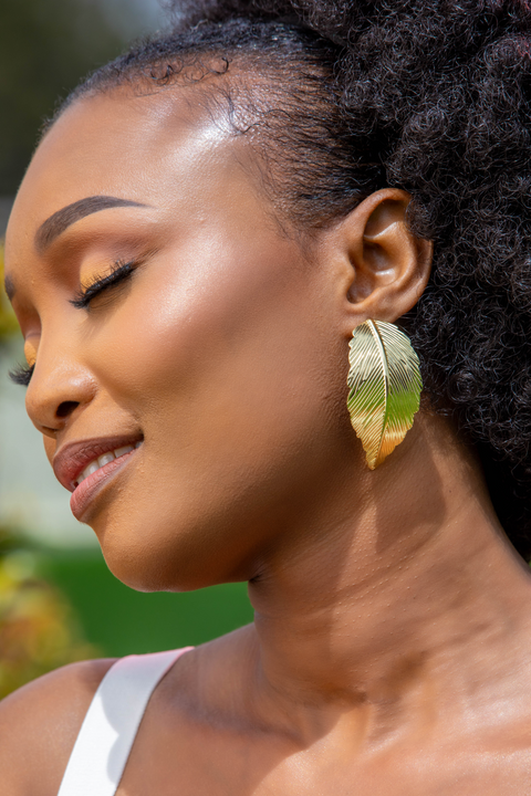 Woman wearing a gold leaf earring with a blurred green background