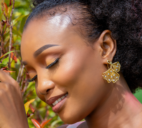 Woman wearing gold earrings and bracelet with a blurred natural background