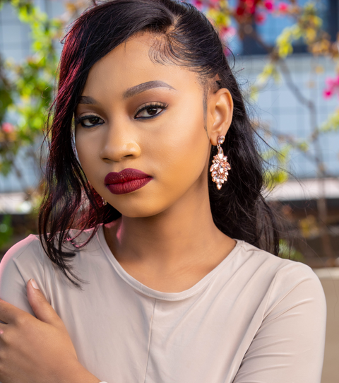 Woman with dark hair and red lipstick wearing a beige top, standing outdoors with blurred background