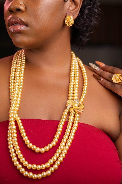 Woman wearing a long gold necklace with matching earrings and ring against a dark background