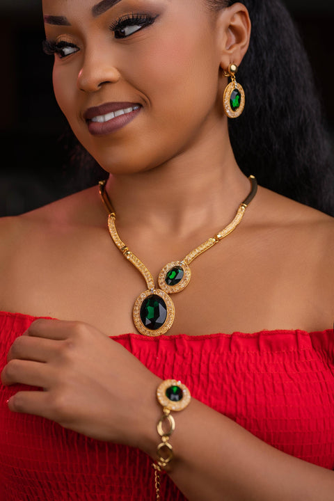 Woman wearing gold jewelry with green gemstones against a dark background