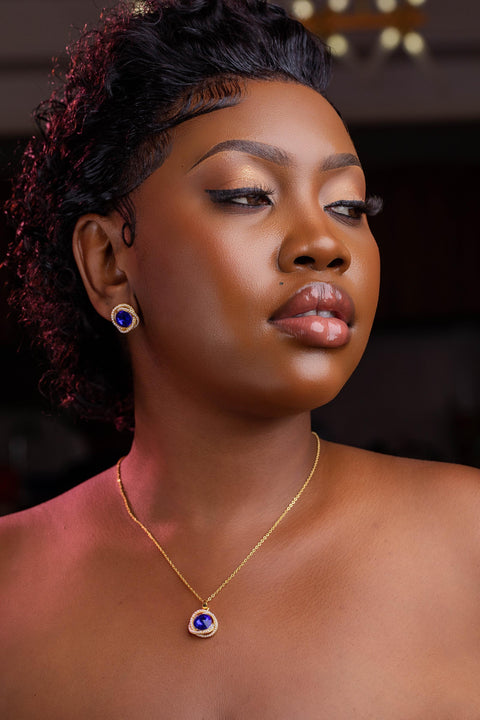 Woman wearing a gold necklace with a blue pendant against a dark background