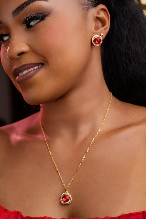 Woman wearing a gold necklace and earrings with red stones.