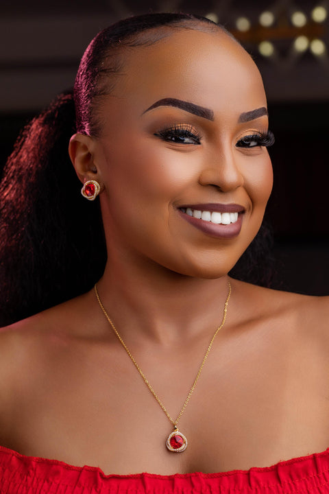 Woman wearing a red off-shoulder top with a necklace and earrings, against a dark background.