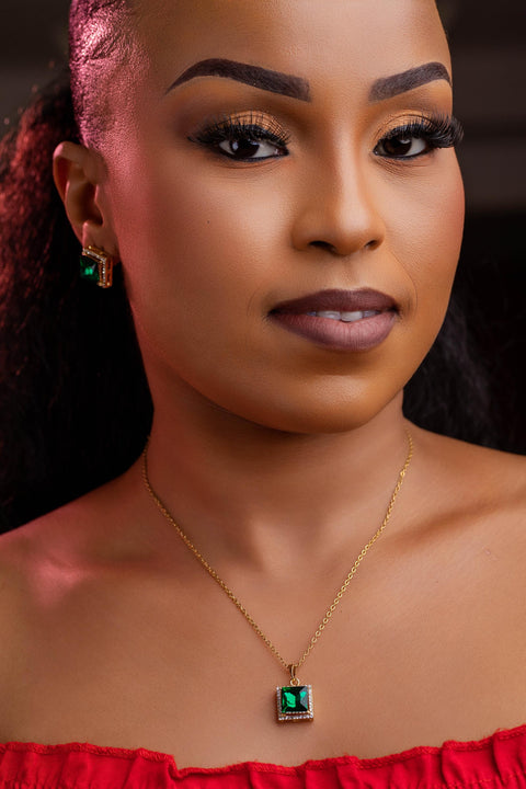 Woman wearing a gold necklace with a green pendant against a dark background
